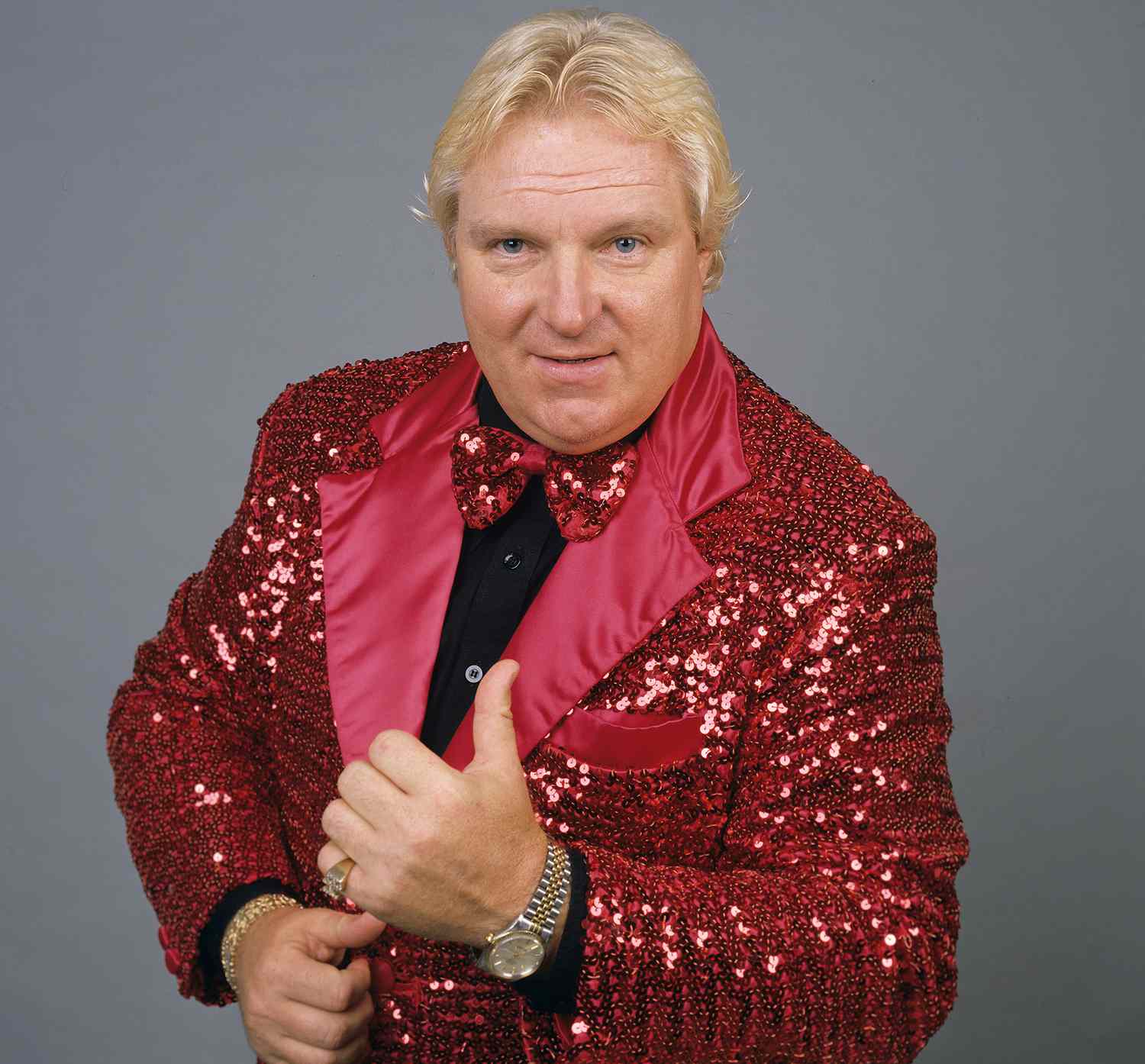Bobby Heenan, giving a thumbs-up with his left hand, smiling, wearing a flashy, red suit.